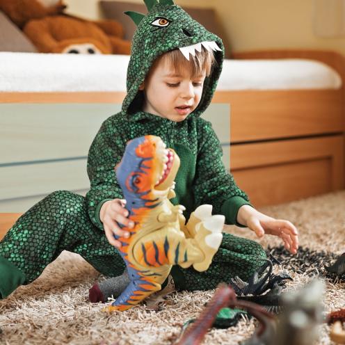En dreng i dinosaurkostume leger med dinosaurfigurer på gulvet. 